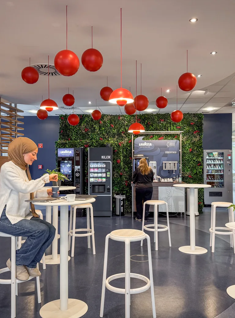 Kaffee-Lounge mit Pflanzenwand und roten Pendelleuchten im Lavazza Professional Office in Verden